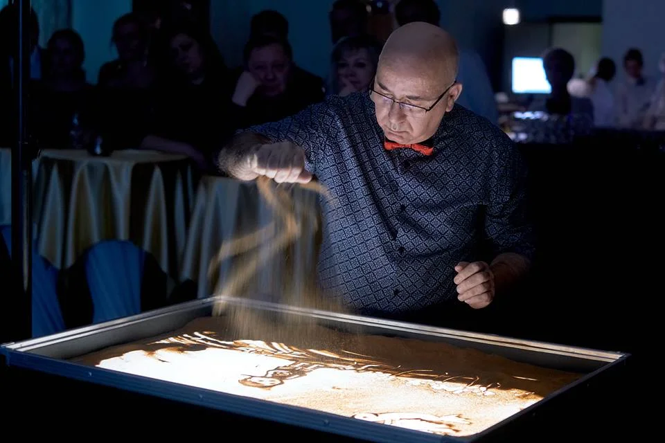 Tigran sypie piasek na podświetlony stół w otoczeniu publiczności